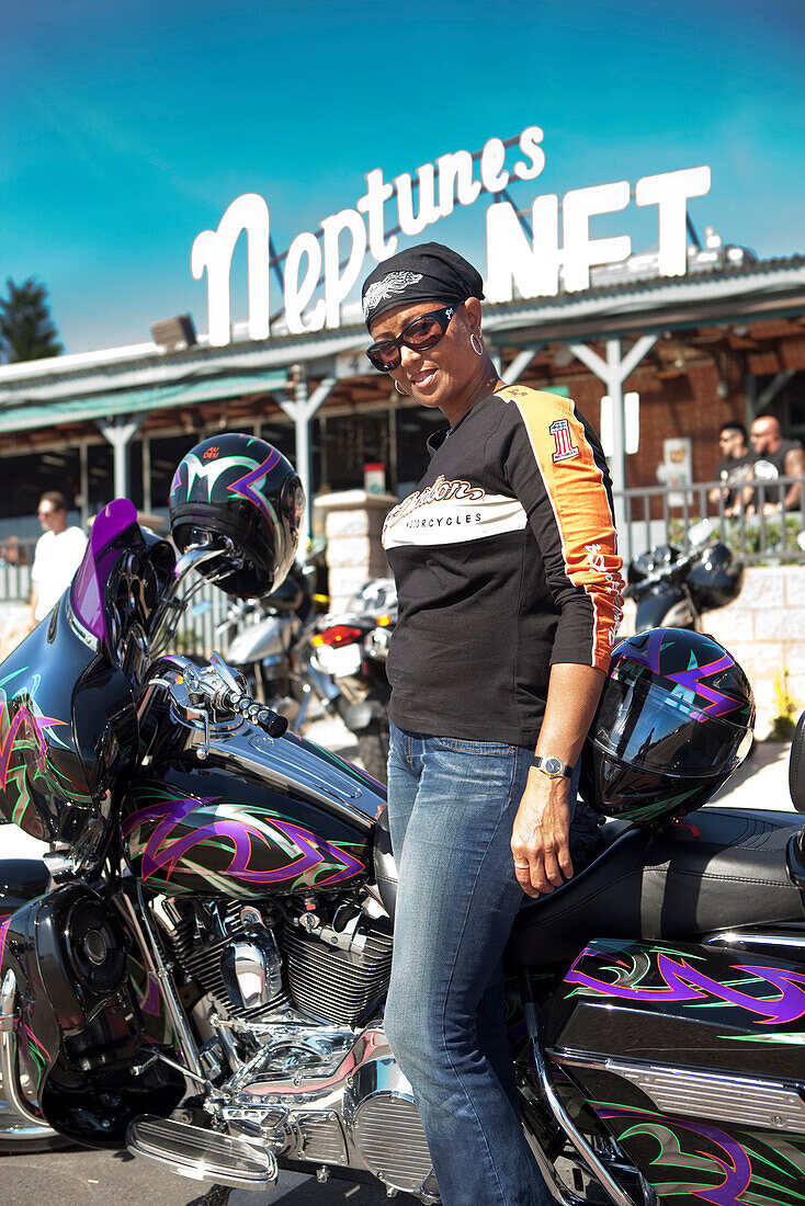 USA, California, Malibu, a biker stands next to her motorcycle in front of Neptunes Net Restaurant on the Pacific Coast Highway