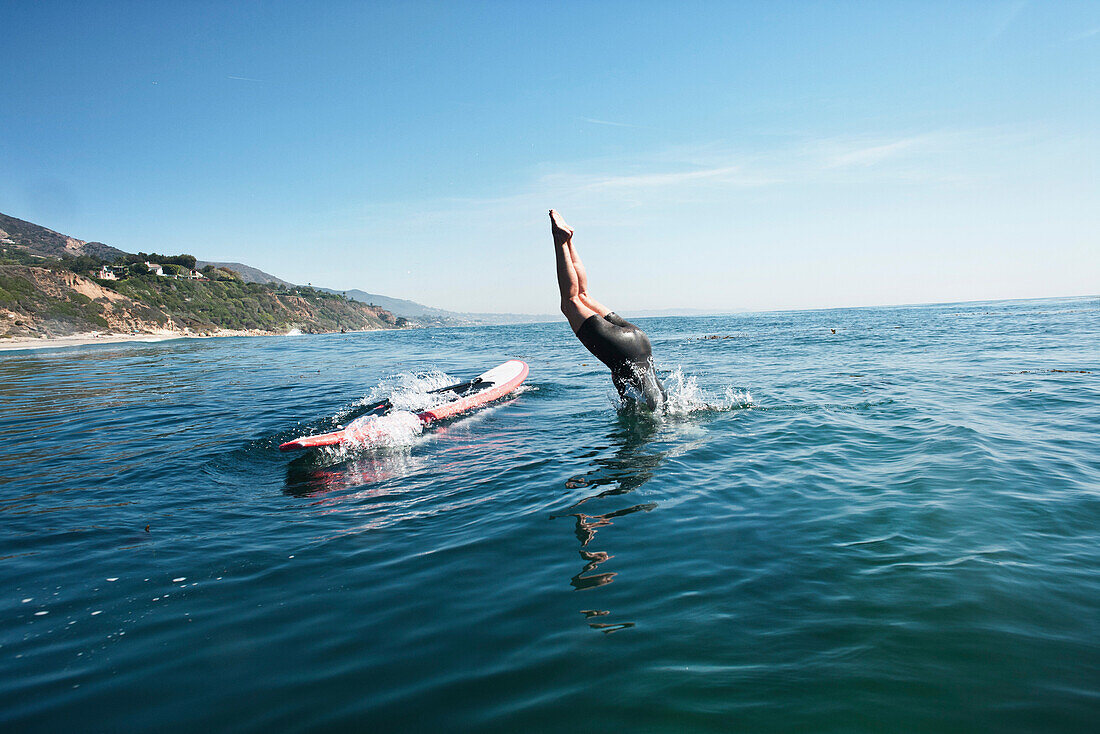 USA, California, Malibu, El Pescador Beach, an athletic woman dives off of her paddleboard into the Pacific Ocean