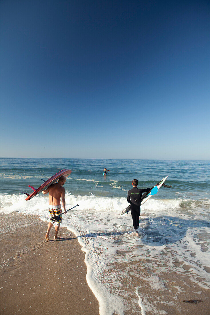 USA, California, Malibu, paddleboarders walk their boards down to the water at Zuma Beach