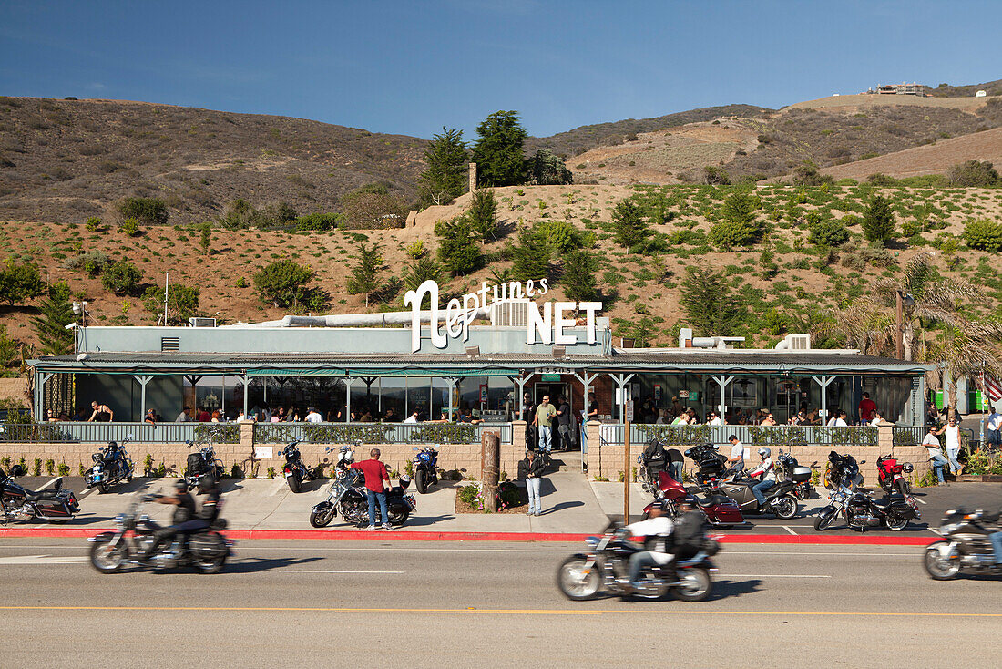 USA, California, Malibu, bikers ride past the front of Neptunes Net Restaurant on the Pacific Coast Highway, the Malibu hills in the distance