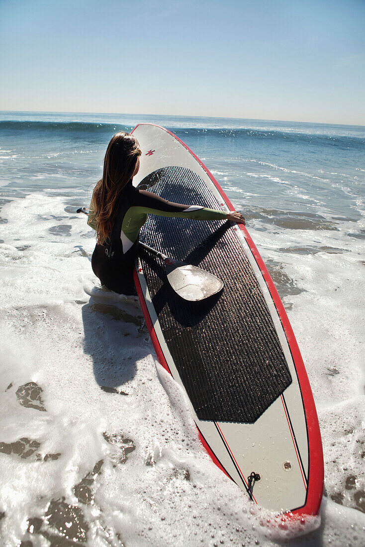 USA, California, Malibu, El Pescador Beach, an athletic woman carries her paddleboard into the Pacific Ocean