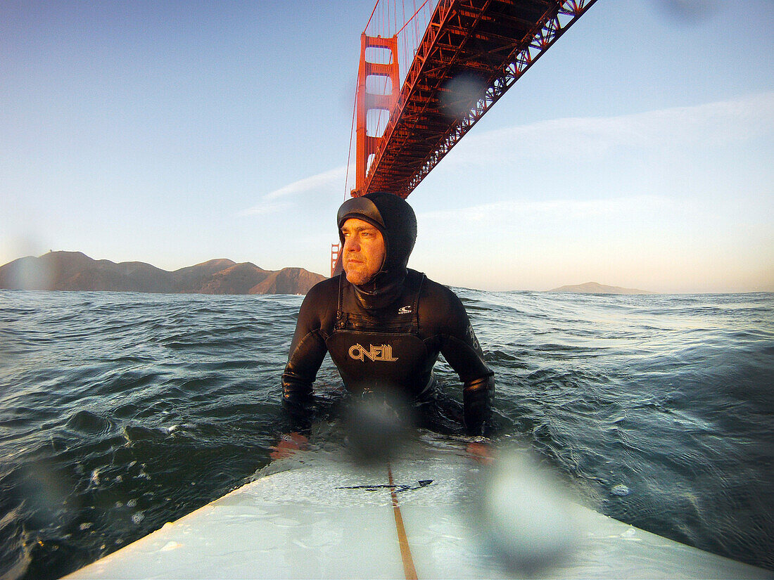 USA, California, San Francisco, Fort Point, surfer sitting on his surfboard under the Golden Gate Bridge at Sunset