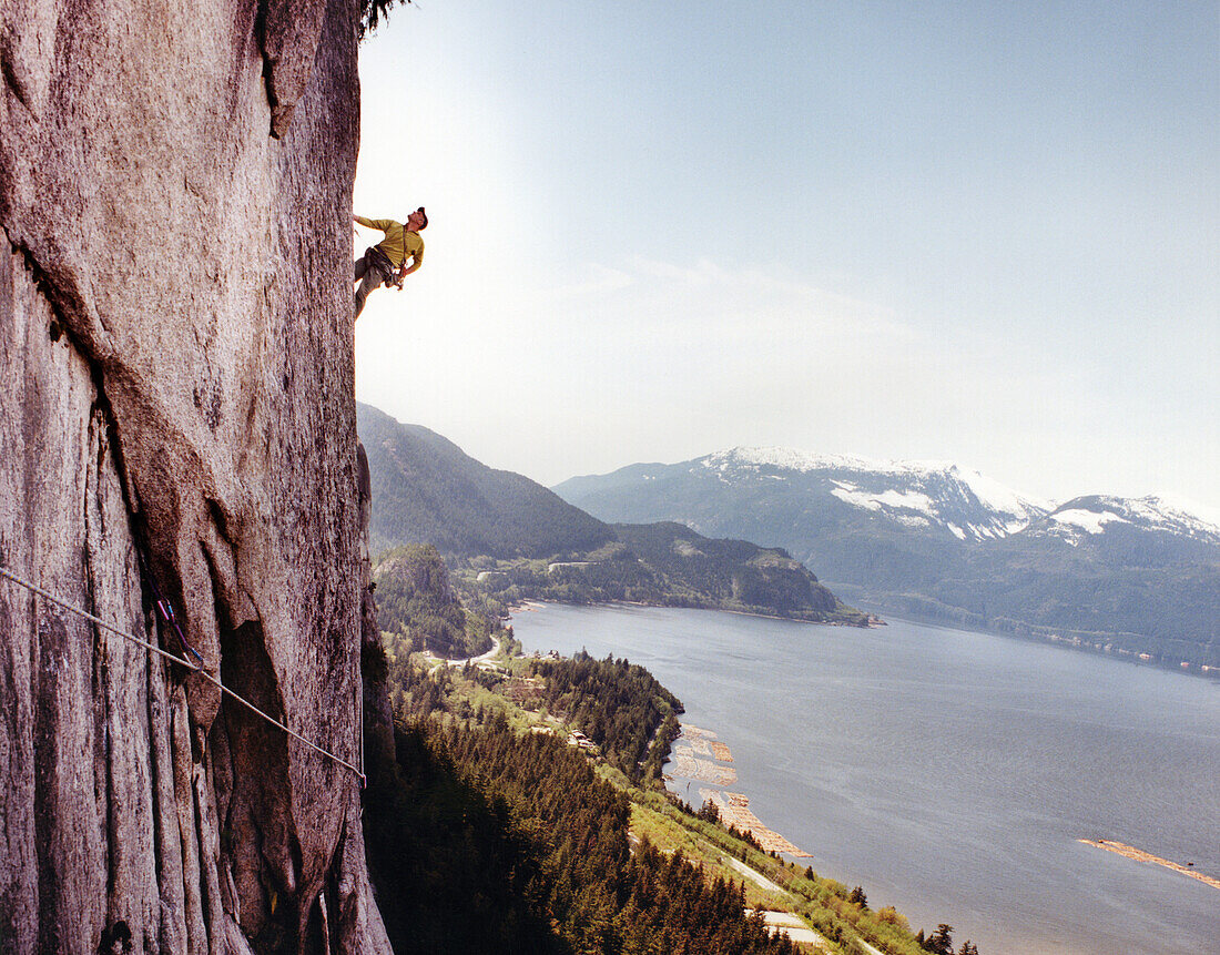 CANADA, man climbing the Stawamus Chief with the Howe Sound in the distance, Squamish, BC