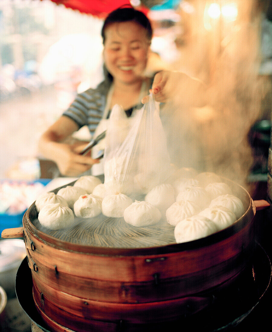 CHINA, Hangzhou, woman cooking steamed buns at market