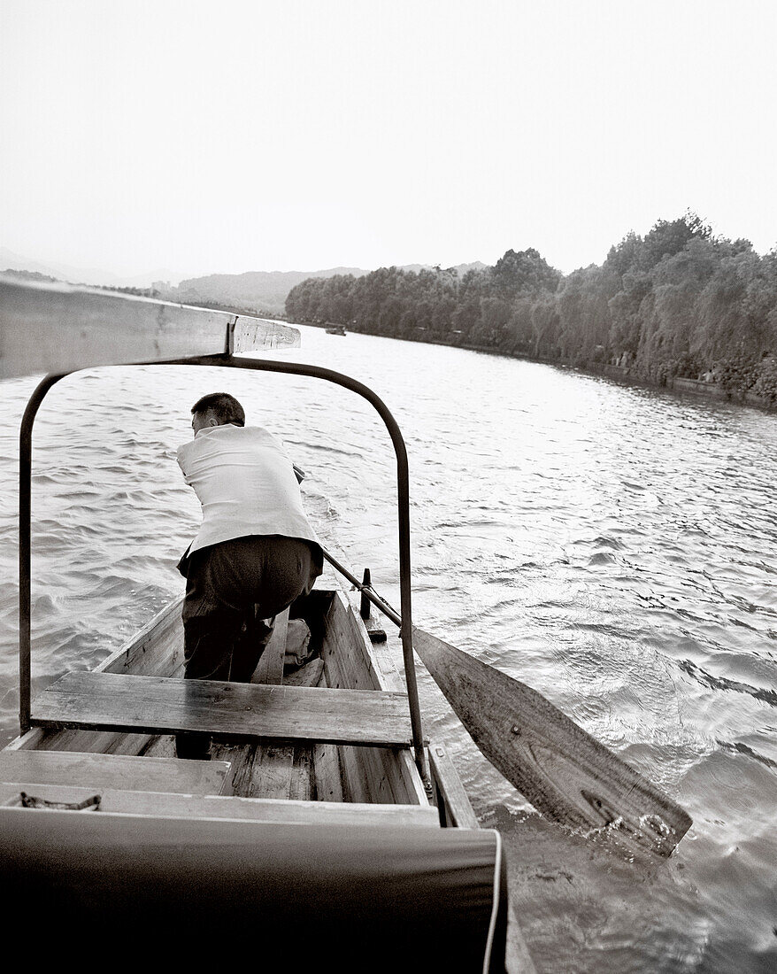 CHINA, Hangzhou, man paddling his boat on West Lake (B&W)