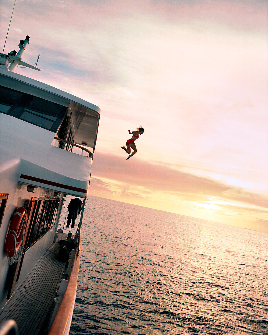 FIJI, Northern Lau Islands, a young woman jumps off of a the top of a yacht into the South Pacific Ocean