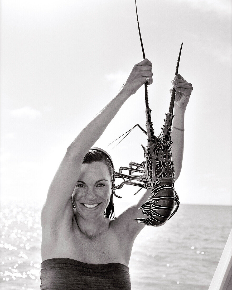 FIJI, Northern Lau Islands, a young woman holds up a freshly caught spiny lobster (B&W)