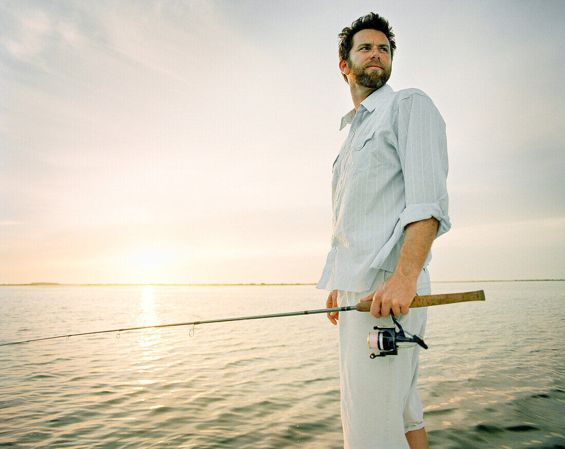 USA, Florida, fisherman holding fishing rod boat at dawn, New Smyrna Beach