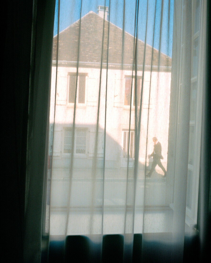 FRANCE, Burgundy, man walking on road seen through window with curtains, Chablis