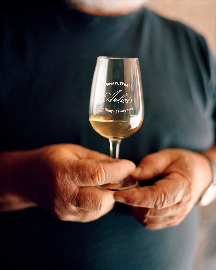 FRANCE, Montigny-les-Arsures, Arbois, Jacques Puffeney stands in his barrel room holding a glass of Vin Jaune, Jacques Puffeney Winery, Jura Wine Region