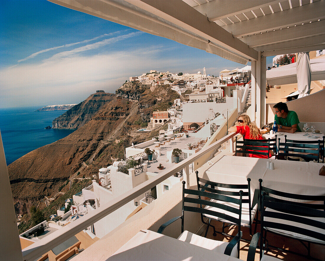 GREECE, Santorini, Fira, a tourist couple enjoys a drink and the view high above the Mediterranean Sea on the island of Santorini