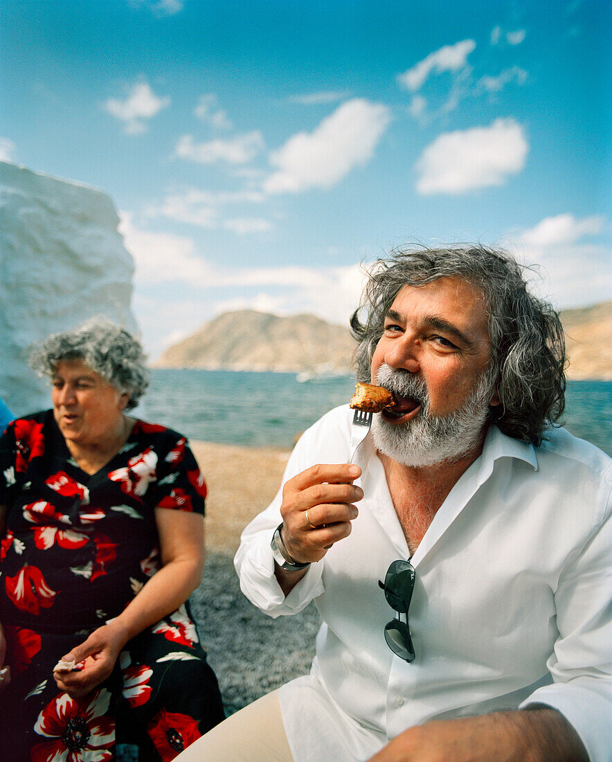 GREECE, Patmos, Diakofti, Dodecanese Island, Kostas enjoys a zucchini ball at Taverna Diakofti by the Agean Sea, the island of Patmos