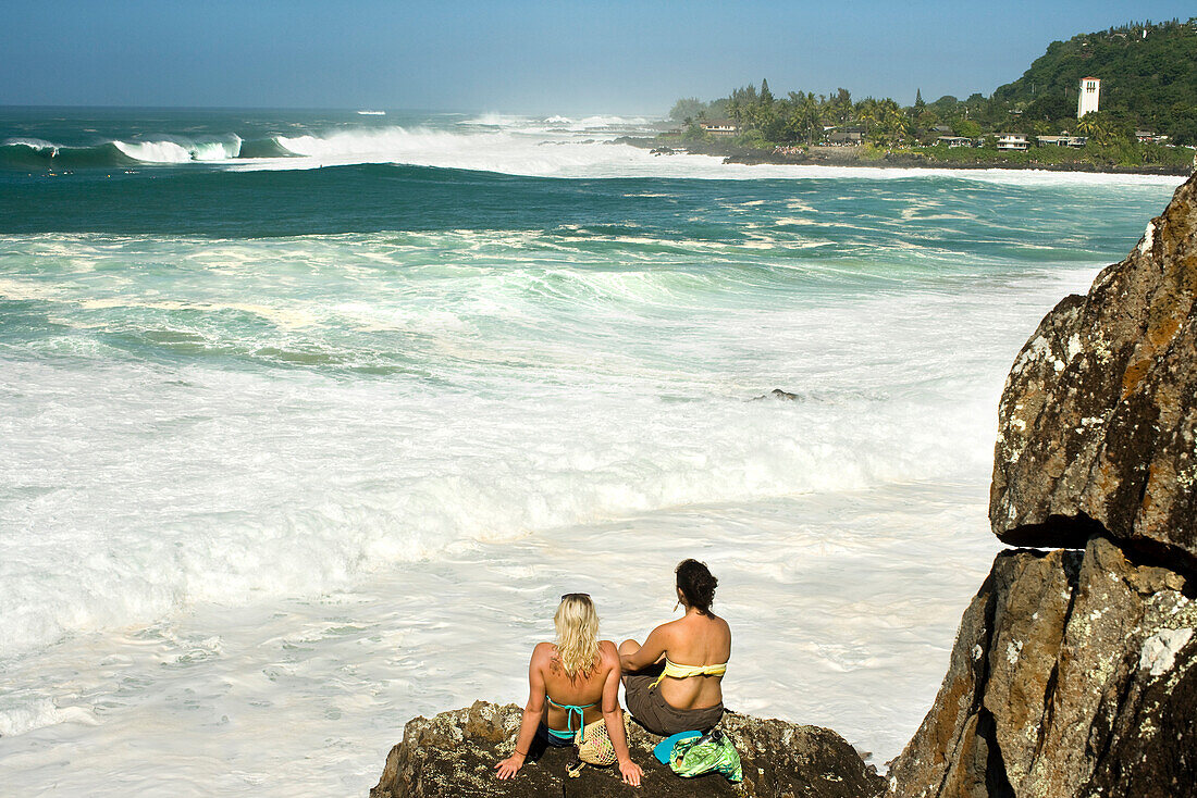 USA, Hawaii, Oahu, the North Shore, young women relax on the rocks and watching the surfing at Waimea Bay