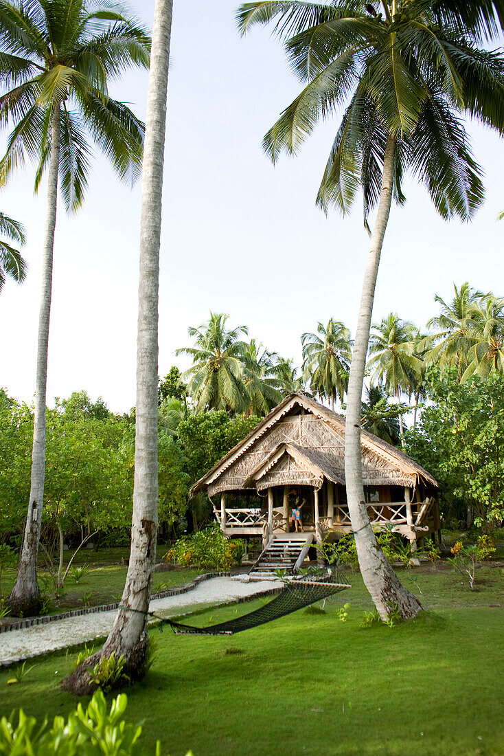 INDONESIA, Mentawai Islands, Kandui Surf Resort, exterior of a guest cabin at Kandui resort with lawn and palm trees