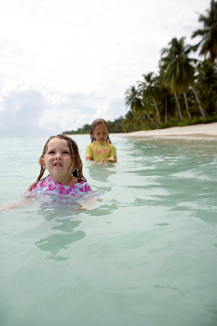 INDONESIA, Mentawai Islands, Kandui Surf Resort, girls playing in the ocean with palm trees in the background