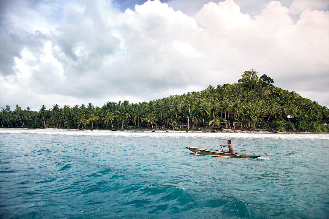 INDONESIA, Mentawai Islands, Kandui Surf Resort, native man in a dugout canoe with palm trees in the background, Indian Ocean