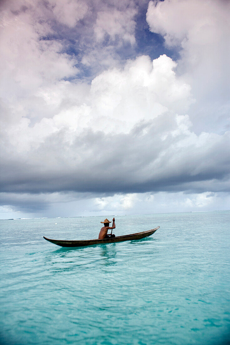 INDONESIA, Mentawai Islands, Kandui Resort, fisherman Gesayas Ges paddling his dugout canoe against a cloudy sky