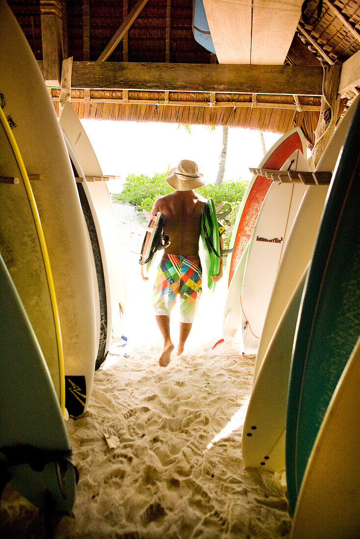 INDONESIA, Mentawai Islands, Kandui Resort, rear view of a man carrying surfboards out of the board storage room