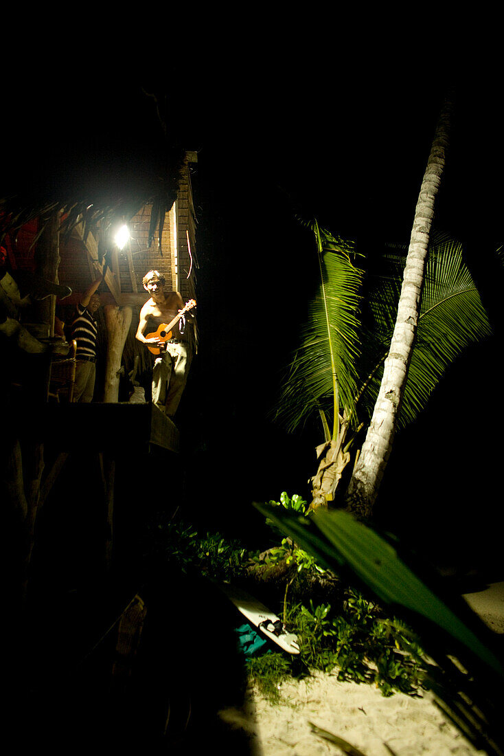 INDONESIA, Mentawai Islands, Kandui Resort, musician playing guitar in a beachside hut at night