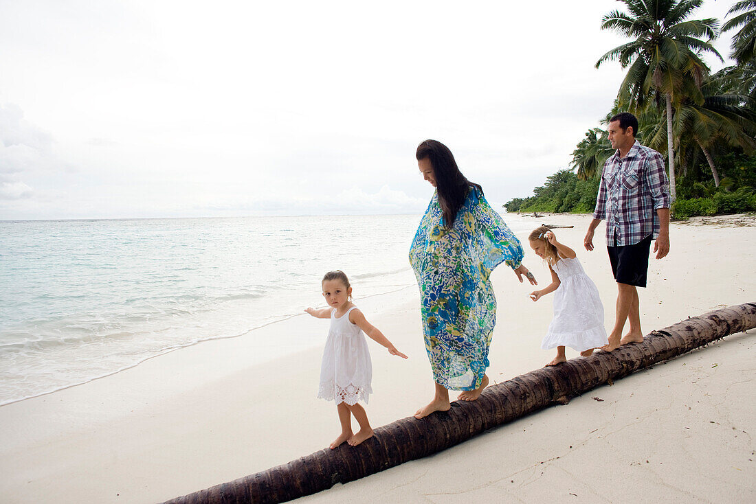INDONESIA, Mentawai Islands, Kandui Resort, family walking and balancing on a fallen palm tree