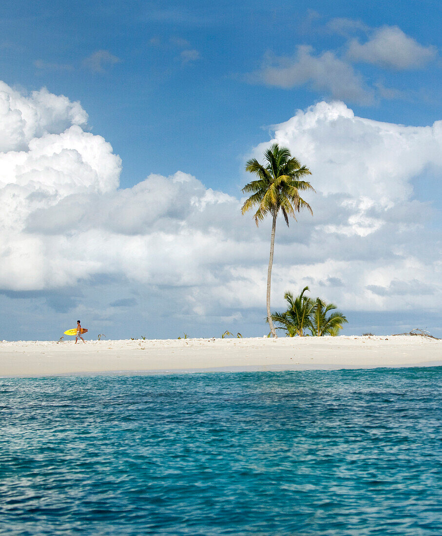 INDONESIA, Mentawai Islands, Kandui Resort, man walking with surfboard on a small island with a palm tree