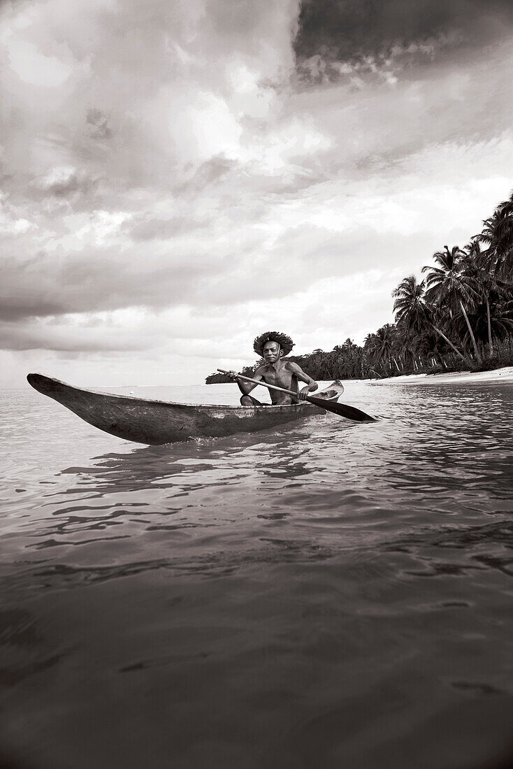 INDONESIA, Mentawai Islands, Kandui Resort, fisherman Gesayas Ges paddling his dugout canoe (B&W)