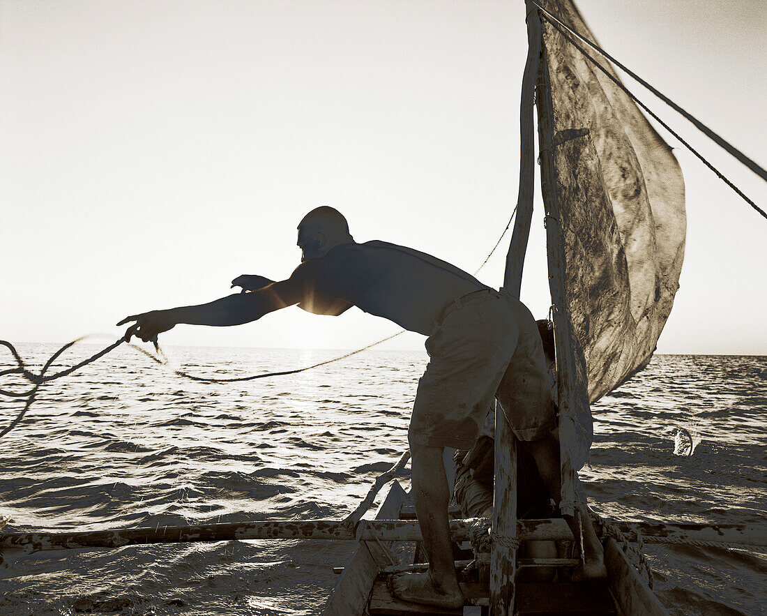 MADAGASCAR, Anjajavy, fisherman in pirogue throwing a rope at dusk