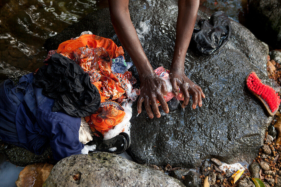 MAURITIUS, Bois Cherie, Mutty Megah (age 63) washes her clothes in a small stream behind her home