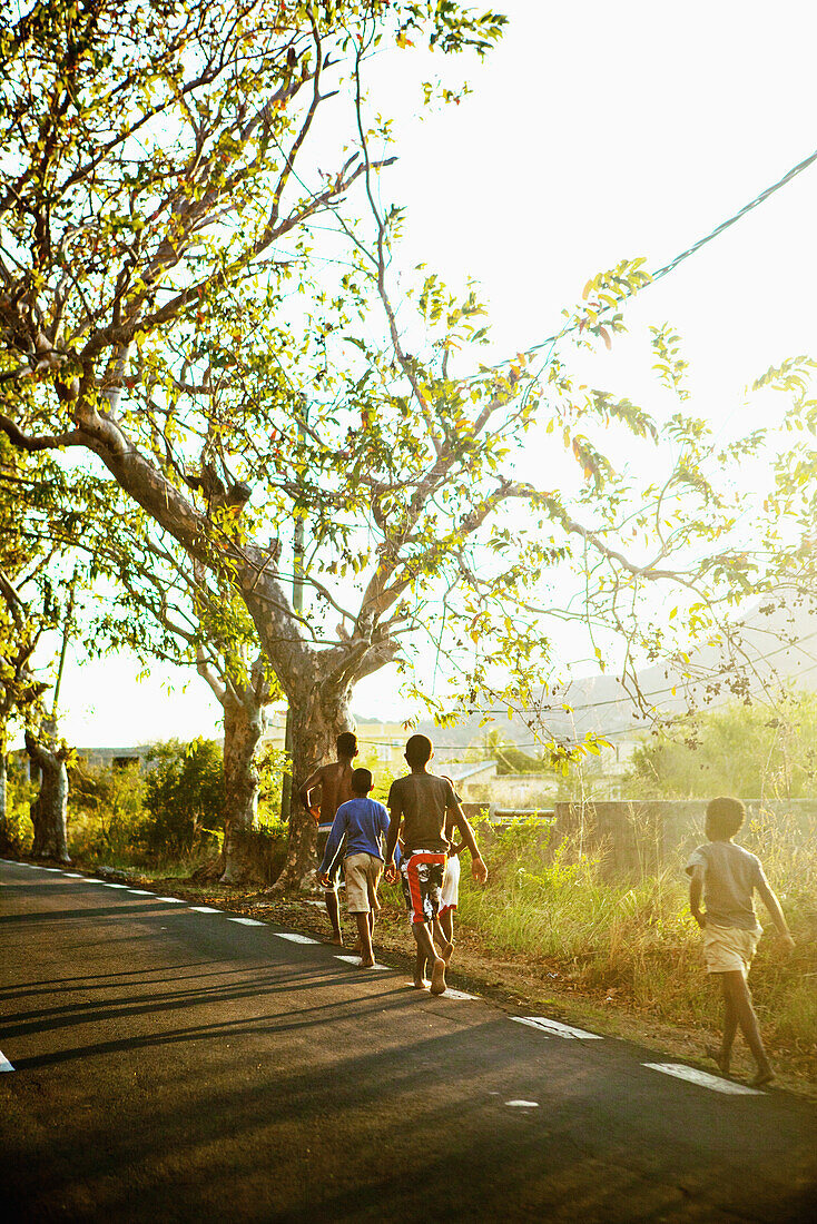 MAURITIUS, boys walk home alongside a main road in rural Mauritius before sundown