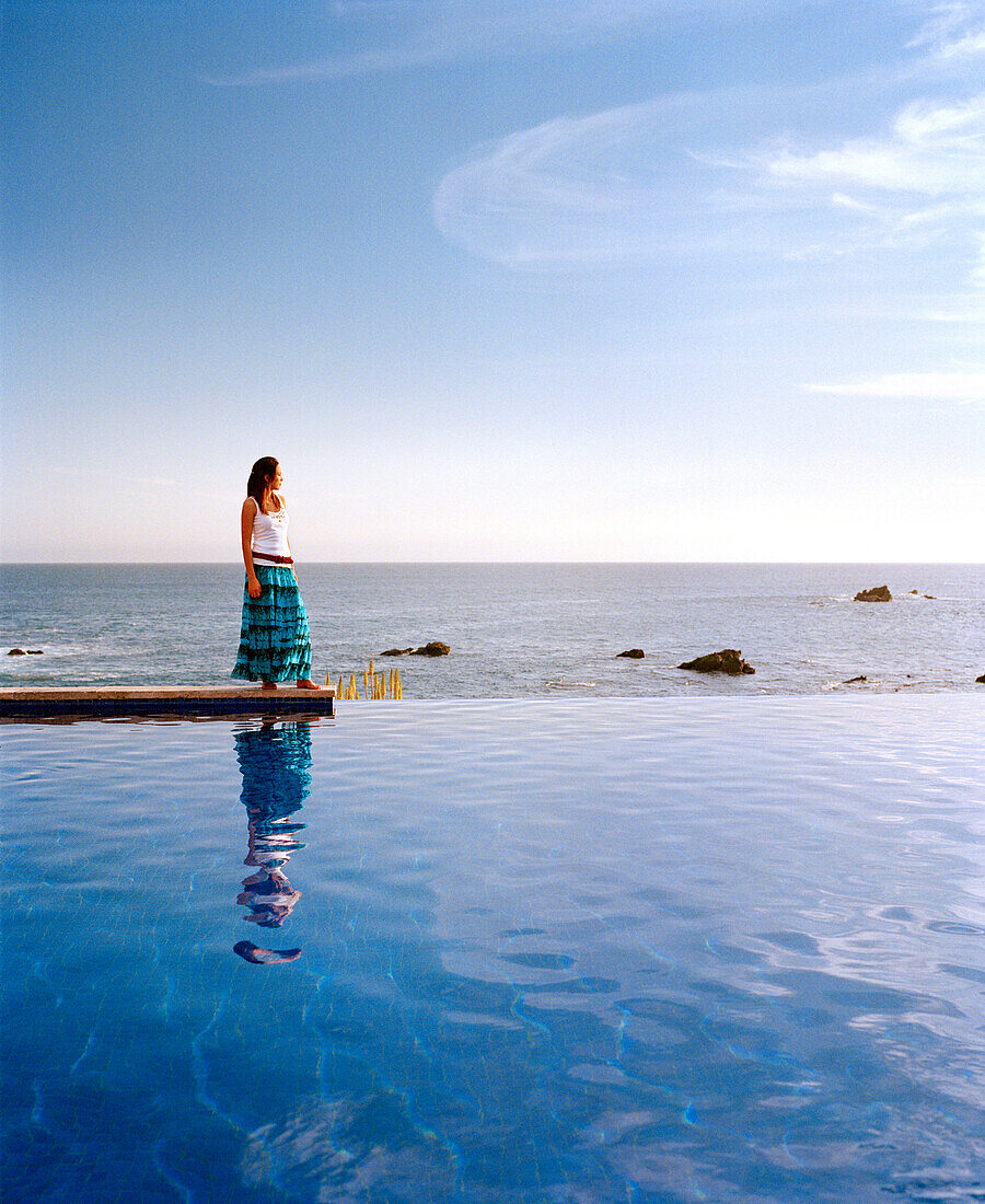 MEXICO, Baja, side view of a woman standing at the edge of an infinity pool, Esperanza Hotel