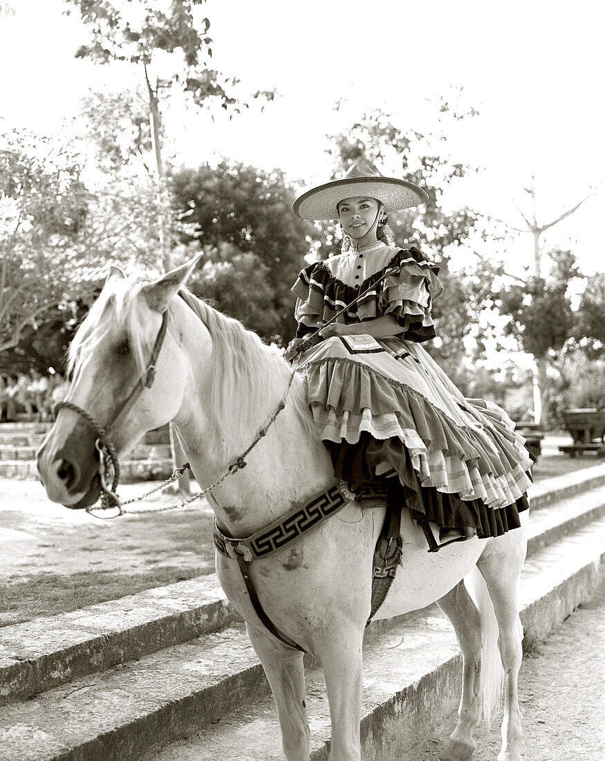 MEXICO, Maya Riviera, Mexican Cowgirl wearing sombrero sitting on horse (B&W)
