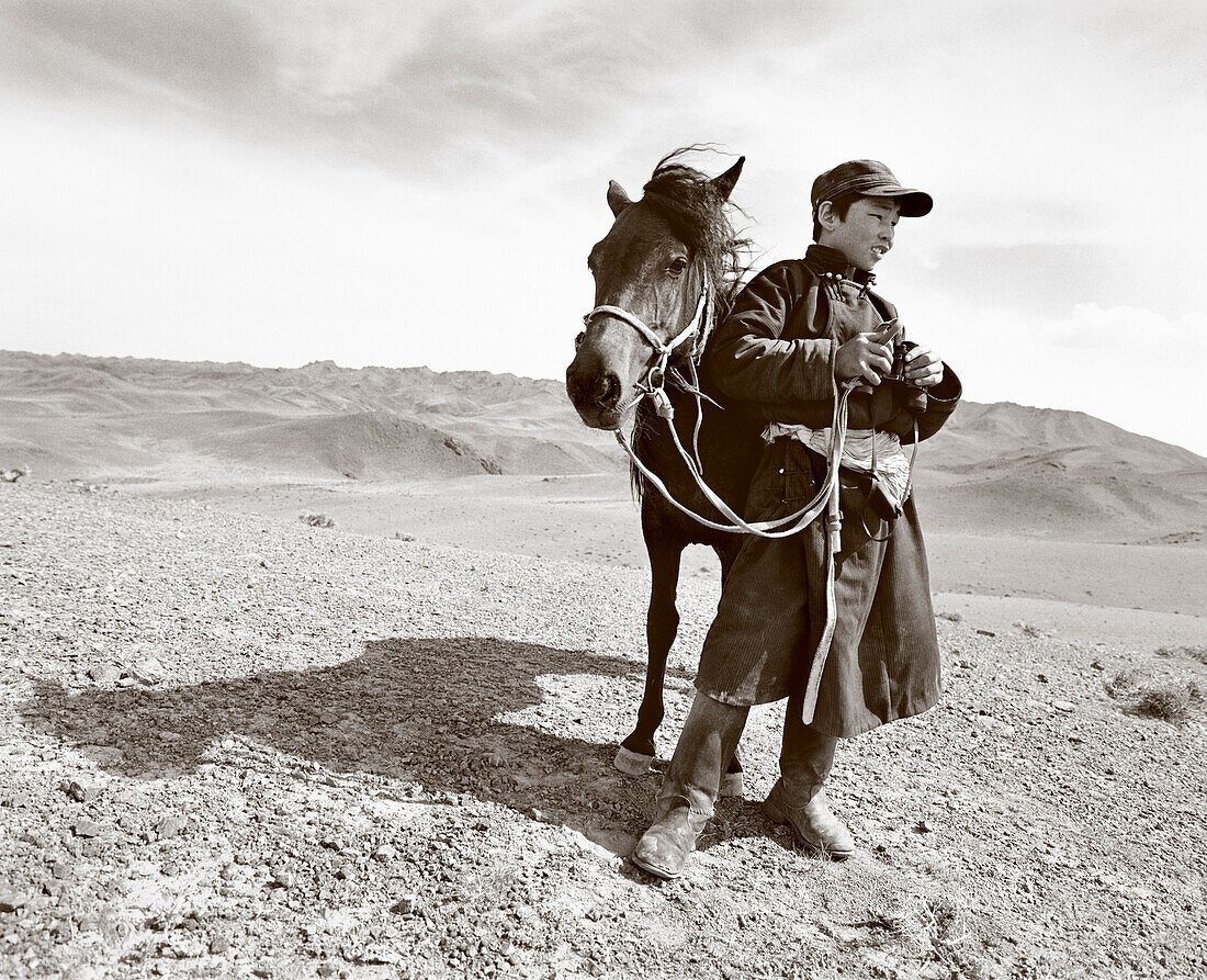 MONGOLIA, shehperd Batsuuriin stands with his horse Khaltar and watches his lifestock, the Gobi Desert, Nemegt Basin (B&W)