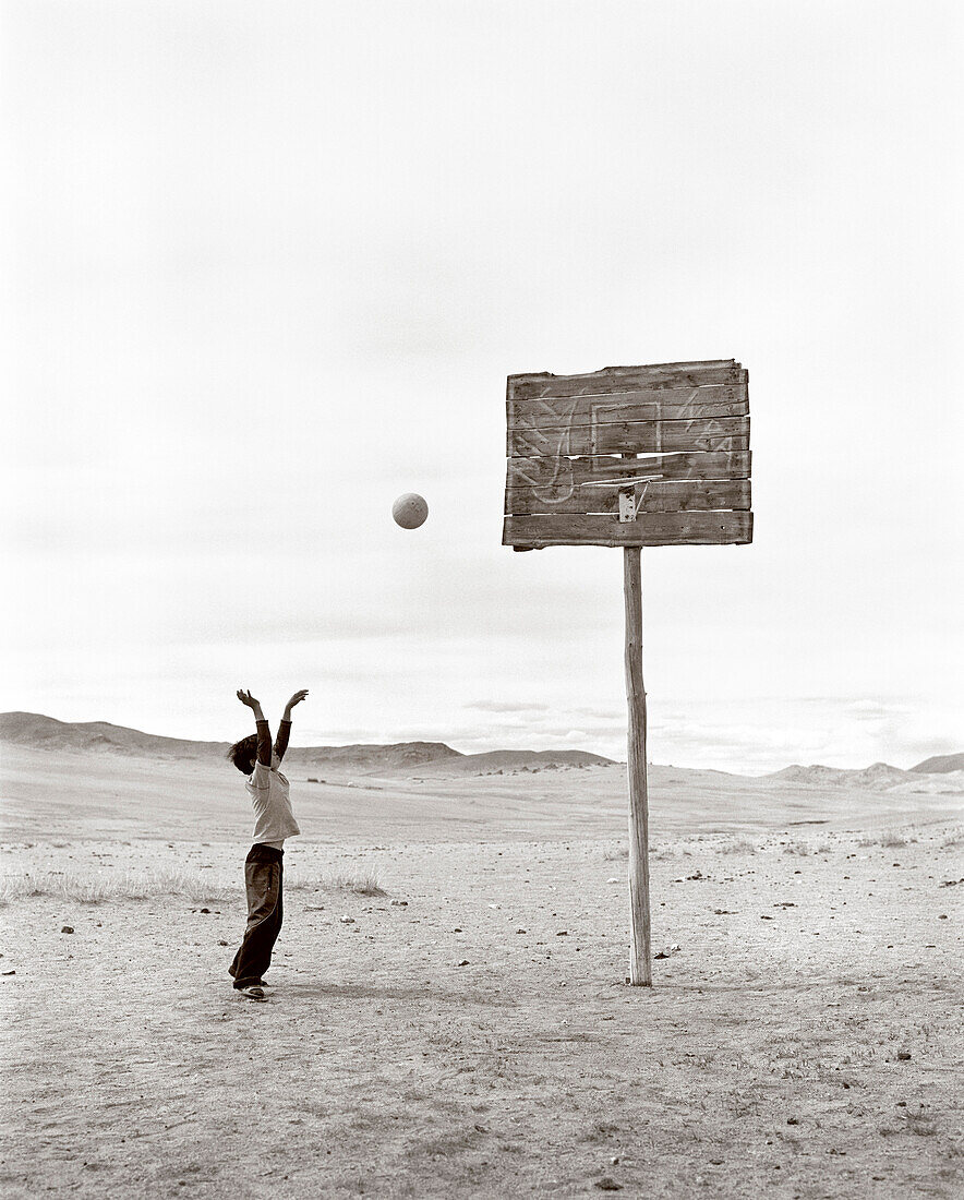 MONGOLIA, Khuvsgul National Park, a young boy shoots a basketball in a wide open barren landscape (B&W)