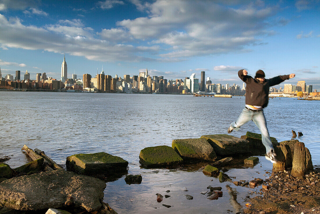 USA, New York, Man jumping the edge of the East River in Brooklyn with the New York City skyline in the distance