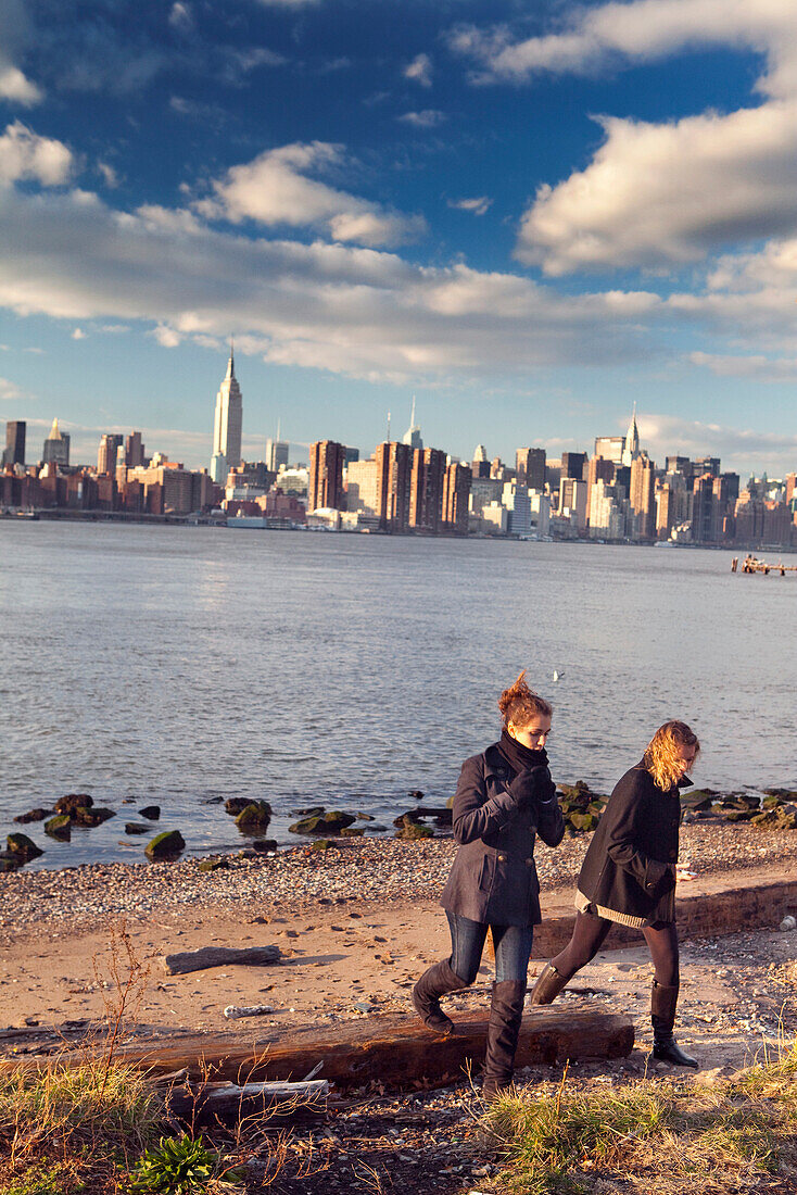 USA, New York, Women walking by the East River in Brooklyn with the New York City skyline in the distance