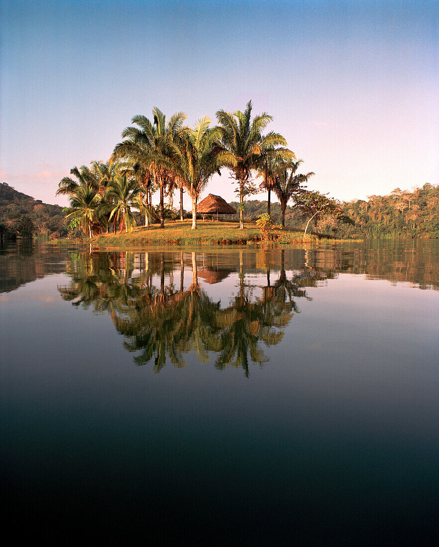 PANAMA, Panama Canal Zone, Barro Colorado, a private island with a single thatched roof hut reflects in the calm water, Central America