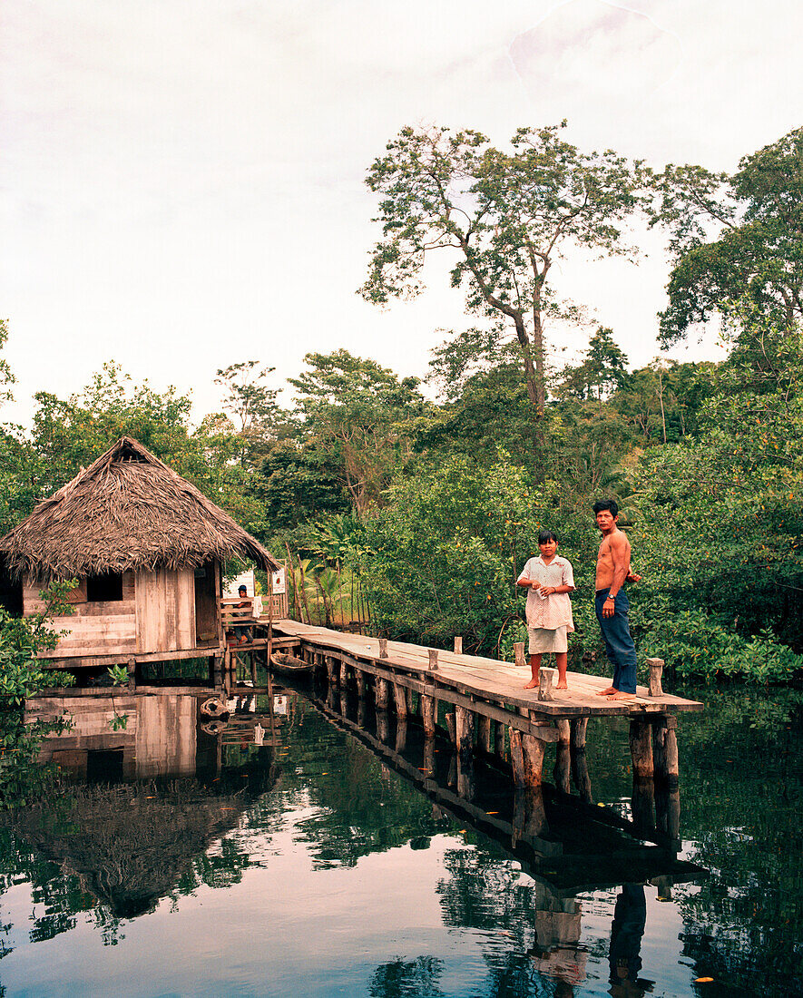 PANAMA, Bocas del Toro, Salt Creek Islands, a Guaymi Indian man and woman stand on a dock in front of their home by the sea , Central America