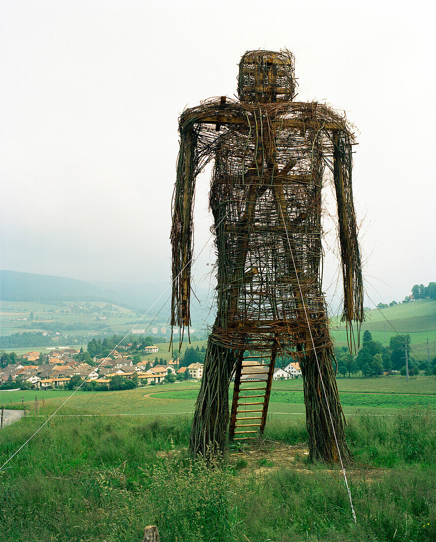SWITZERLAND, Motiers, a sculpture of a figure made of wood and branches adorns the hillside above town, Jura Region