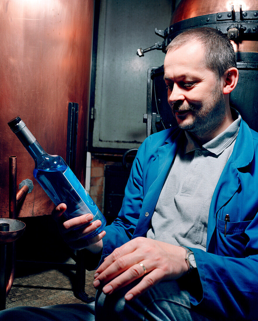 SWITZERLAND, Couvet, Absinthe maker Claude-Alain Bugnon holding a bottle at his Artemisia Distillerie, Jura Region