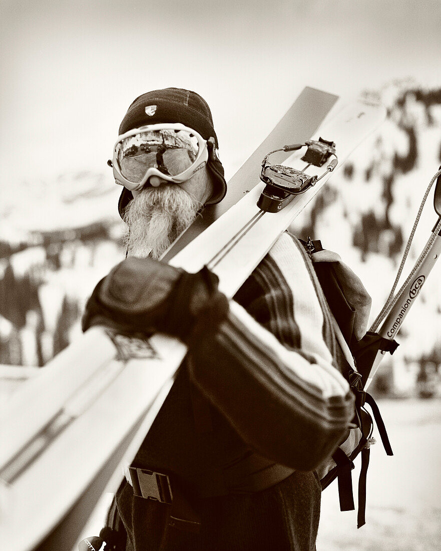 USA, Utah, male telemark skier carrying skis on his shoulder (B&W)