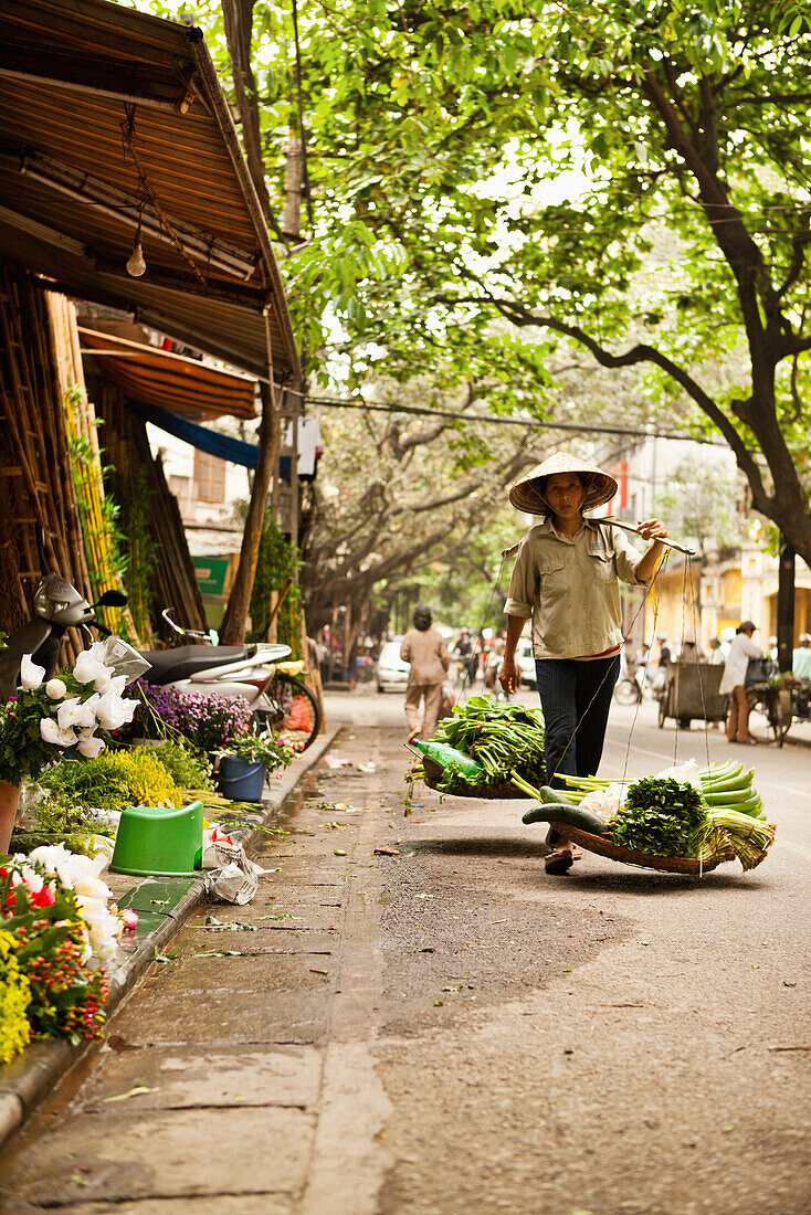 VIETNAM, Hanoi, a street scene of a woman walking down the street selling her produce