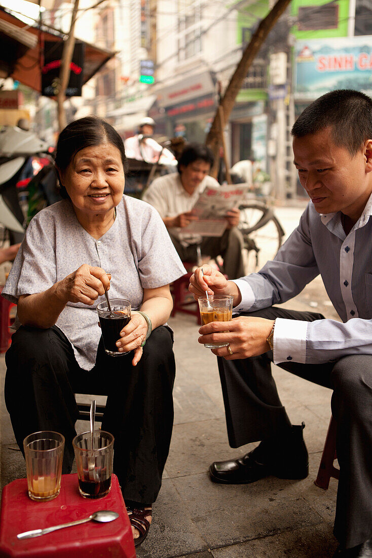 VIETNAM, Hanoi, Miss Thai the owner of Cafe Nang sits on the sidewalk in front of her coffee shop in the Old quarter