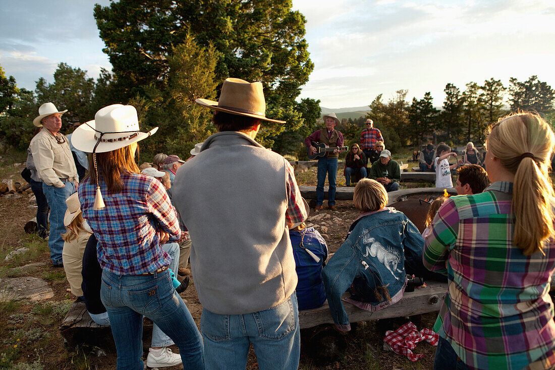 USA, Wyoming, Encampment, guests at a dude ranch sit around a campfire and listen to a man play the guitar and sing country western songs, Abara Ranch