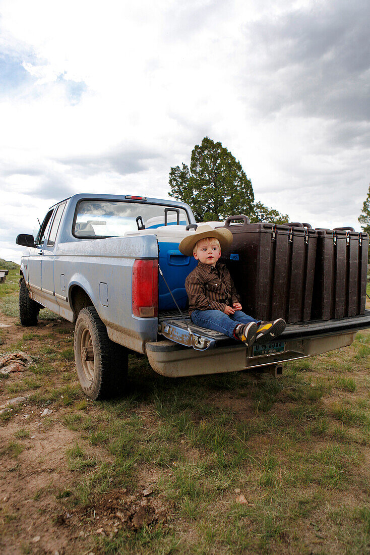 USA, Wyoming, Encampment, a little boy in a cowboy hat sits on the back of a pickup truck, Big Creek Ranch
