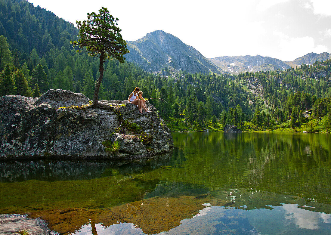 Young people sitting on a rock at lake Dieslingsee, Turracher Hoehe, Styria, Austria