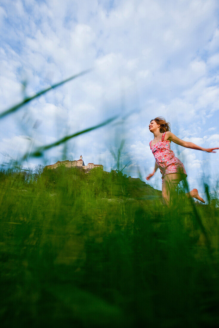 Young woman running over a meadow, Riegersburg castle in background, Styria, Austria