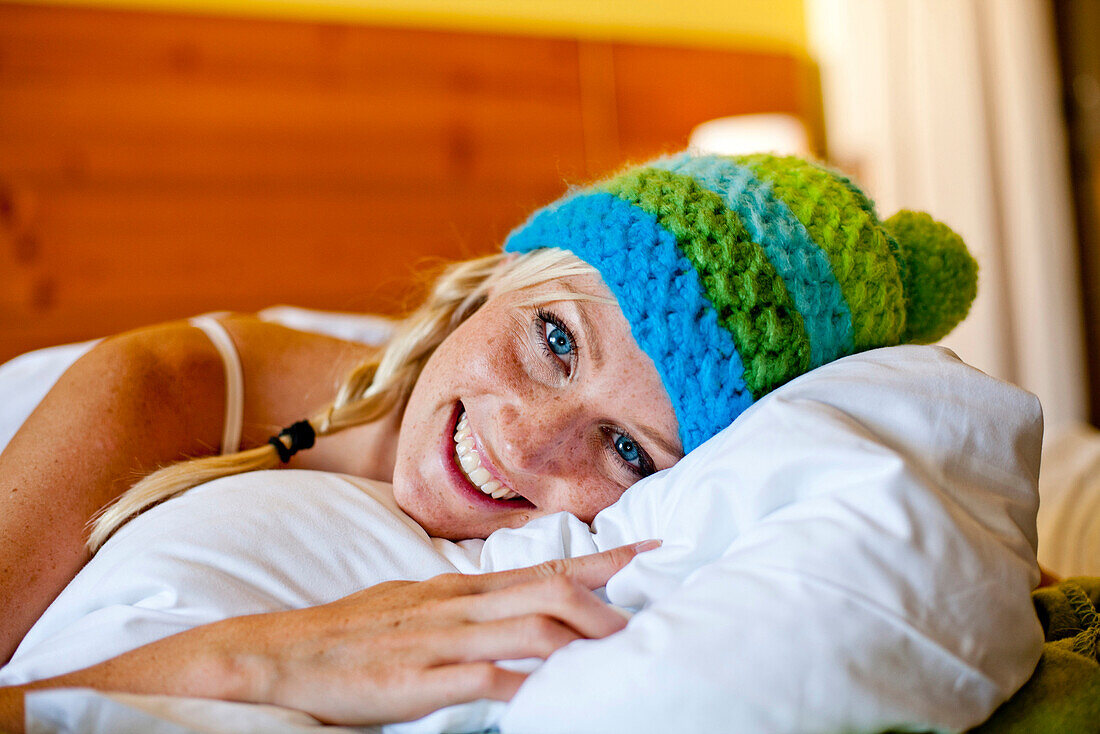 Young woman wearing a wolly hat lying in a bed, Fladnitz an der Teichalm, Styria, Austria