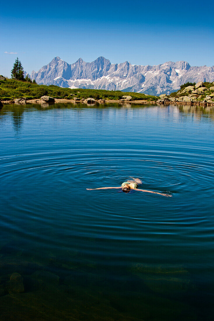 Person bathing in lake Spiegelsee, Dachstein mountains in background, Styria, Austria