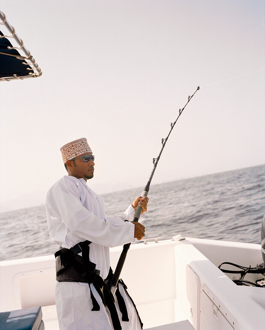 OMAN, Muscat, young man in traditional clothing fishing on boat