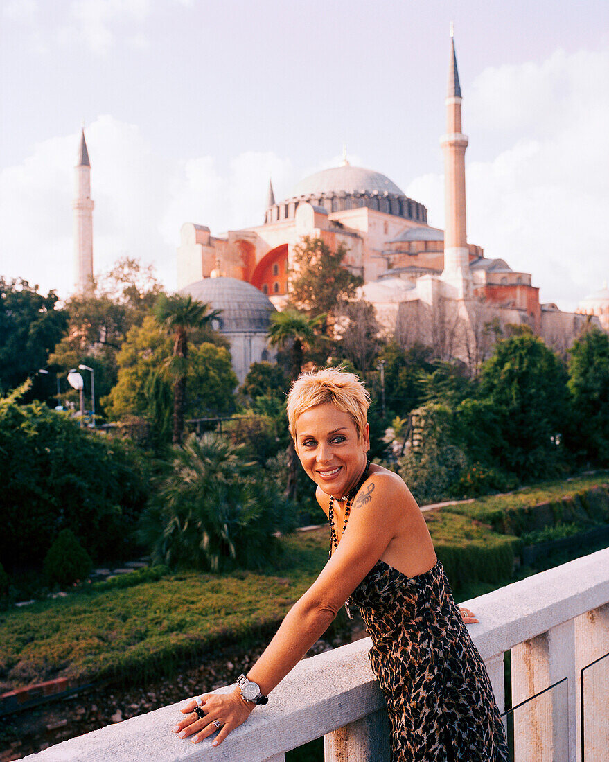 TURKEY, Istanbul, smiling lady looking away with the Aya Sofya mosque in the background. She is standing on the roof balcony of the Four Seasons Hotel.